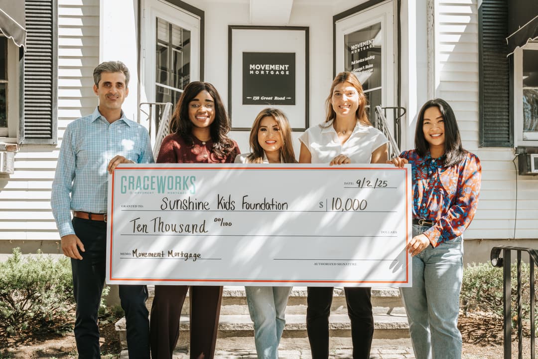 The Elle Group present a $10,000 Movement Mortgage check to Sunshine Kids on office steps—feature photo underscoring the partnership highlighted in the article.
