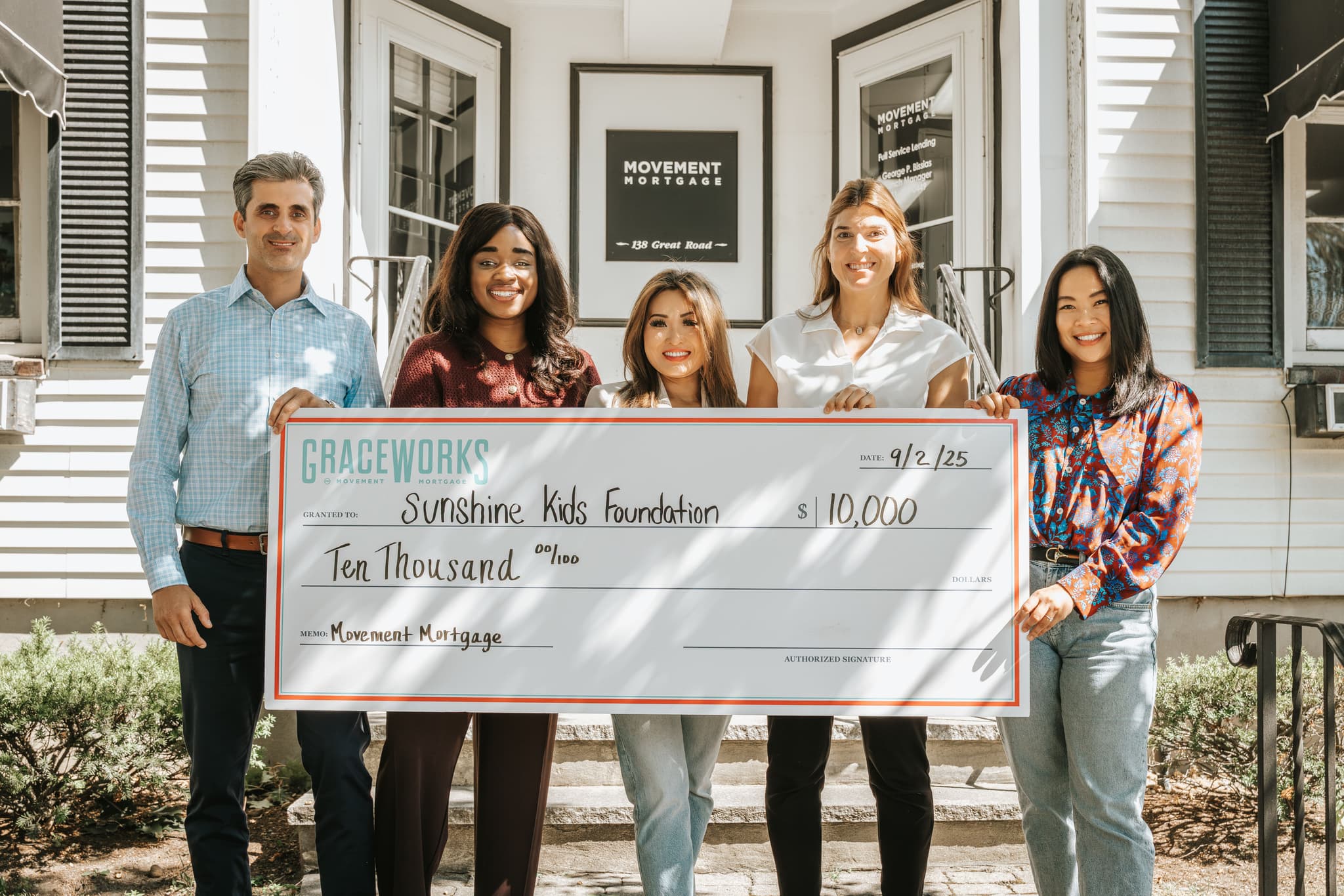 The Elle Group present a $10,000 Movement Mortgage check to Sunshine Kids on office steps—feature photo underscoring the partnership highlighted in the article.